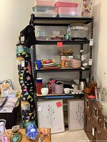 Black metal shelving unit against a wall with various household items on and around shelves.