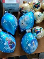 Blue Disney Frozen character ornaments and cream Thomas Kinkade village-themed balls
