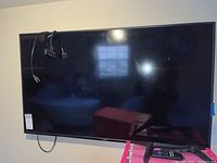 Front view of 50 inch Vizio TV mounted on wall with Roku device and cables hanging on side. Pink storage container, remotes on TV legs in front.