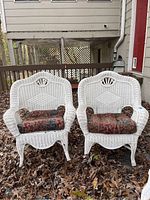 Front view of two white wicker chairs with patterned cushions on a deck covered with leaves