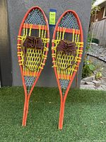 Full view of the pair of vintage adult snowshoes leaning against a wall outdoors on grass.