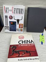 Three hardcover art reference books arranged on a table: 'Art of Our Century,' 'China: A History in Art,' and a plain dark hardcover book identified as 'The Illustrated History of Antiques'