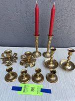 Full view of all brass candle holders arranged on cloth background showing 3 pairs and a set of 4, tallest pair has red taper candles.