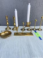 Full view of all eight brass items arranged on white fabric against gray wall