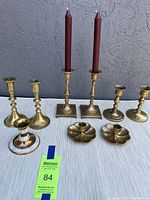 Front view of all 9 assorted brass candlestick holders arranged by pairs and single with candles in the tallest pair
