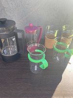 Photo showing two Bodum French presses (black 4-cup and purple individual) with two vintage green Bodum coffee mugs and two cork base floating candle holders.