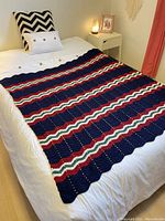 Full view of crocheted afghan blanket laid flat on a white bed.