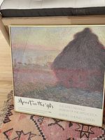 Full front view of framed Monet exhibition poster showing the haystack and landscape scene with text at bottom.