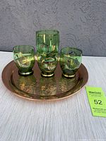Hammered copper tray with four green vintage glasses with gold and red decorations arranged on it.