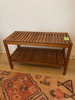 Full view of walnut slatted bench against a white wall, positioned on patterned rug showing size and overall condition.