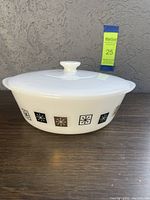 Side view of the white glass casserole with retro Atomic Snowflake pattern in black and brown squares around the rim and fitted white lid with knob.