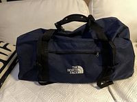 Full view of large navy blue The North Face duffel bag with black handles and front zippered pocket, showing embroidered white logo.