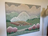 Full frontal image of large quilted textile art depicting a landscape with hills, pink blossom trees, houses, and clouds.