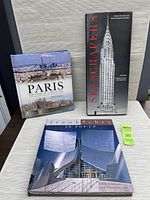 Three hardcover novelty pop-up books titled 'Paris: The Story of a Great City', 'Skyscrapers', and 'Frank Gehry In Pop-Up' arranged on a flat surface.