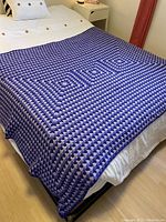 Full view of handmade purple crocheted afghan blanket spread on a bed showing overall pattern and size.