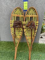 Front view of the pair of small vintage wooden snowshoes with yellow twisted rope webbing and leather lace bindings.