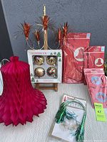 Seven vintage Alderbrook Christmas decorations displayed including red honeycomb bells, green tinsel chandelier, boxed ornaments, and unopened packages of various vintage paper decorations.