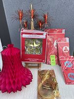 Photo of the multicolour tinsel star tree-topper in original packaging, several packages of red paper honeycomb accordion bells in varying sizes, and the vintage gold tinsel chandelier in sealed bag all on a surface.