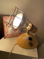 Yellow GE reflector sunlamp with large reflector bulb and metal wire cage on a table with original bulb inside.