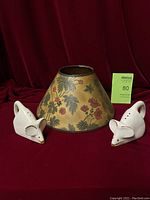View of two white ceramic mouse salt and pepper shakers positioned on either side of a floral patterned lampshade on a red backdrop.