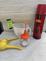 Vintage Thermos, Tupperware measuring cup, kitchen chopper, and lemon press displayed