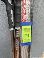 Two Atomic ski poles held vertically showing grip and shaft details along with MaxSold auction tag attached