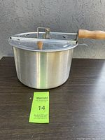 Full view of aluminum Whirley Pop popcorn popper with lid and wooden handle, displayed on table.