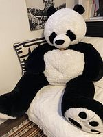 Full view of large stuffed panda sitting on a couch showing white and black plush fur and detail of paws