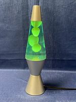 Front view of the 14.5 inch lamp with gold base and green wax blobs suspended in clear liquid against a blue background.