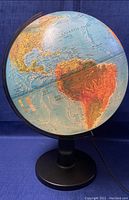 Side view of the lighted world globe showing North and South America with a partially illuminated surface attached to a black stand.
