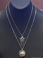 Two sterling silver necklaces displayed on a black jewelry bust, showing the pendants and chains clearly.