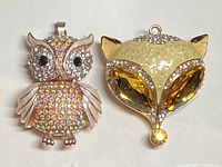 Front view of both pendants together showing owl on left and fox on right with crystals and metal details
