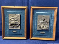 Pair of framed vintage 3D pewter wall art plaques featuring sailing ships on blue fabric background and wood frames.