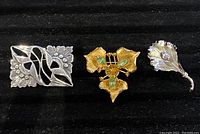 Three sterling silver brooches arranged side by side on black fabric background