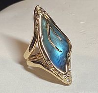 Angled close-up of gold-toned ring with a blue lucite stone and rhinestone accents.