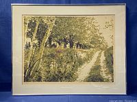 Framed landscape print showing a tree-lined dirt road on textured paper with mat and frame.