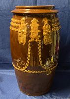 Front view showing detailed raised relief decorations including human figures and pagoda motif on large brown glazed clay pot.