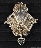 Front view of the silver plated Art Deco brooch showing 3D cherub figures, shell motif, roses with pearl-like centers, and dangling heart-shaped gem.