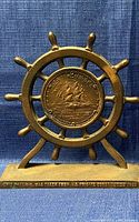 Single metal bookend shaped as ship's wheel with USS Constitution medallion and base inscription.