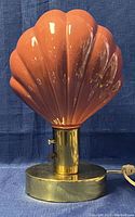 Front view of lamp showing pink scalloped shell shade on brass base