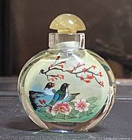 Front view of the glass opium snuff bottle showing paintings of two birds on a branch with red blossoms and pink flowers below.