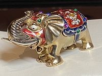Side angle showing gold tone metal elephant with multicolored enamel and crystals on back wearing decorative saddle embellishment.