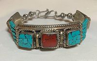 Front view of the bracelet showing three large stones, turquoise-coral-turquoise, set in silver-tone frames with twisted rope detailing and turquoise beaded strands.