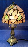 Lamp lit, showing the Tiffany style stained glass shade with floral design and metal ornate base on dark background.