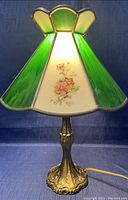 Front view of the lamp lit showing green stained glass panels and floral design on white panels