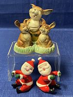Two sets of salt and pepper shakers: a triple bunny set and a pair of Santa Claus figures, all porcelain and vintage.