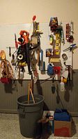 Photo showing pegboard with various hand tools hanging: hammer, pliers, screwdrivers, clamps, tape measure, levels, and power tools including Black and Decker blower and chainsaw.