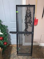 Full view of black metal expanded mesh bumper storage rack with attached coiled bungee net hanging on front.