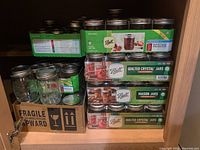 Overall view of canning jars stacked inside a cabinet showing three sealed boxes of Ball canning jars and some loose jars in a cardboard box.