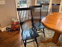 Four black wooden spindle-back chairs lined up next to dining table and windows